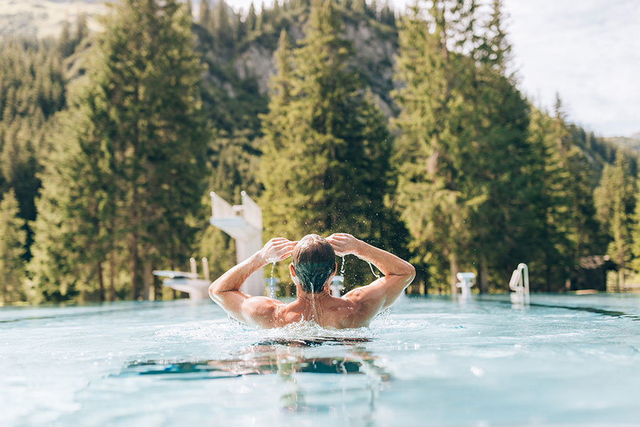Person swimming in an outdoor pool with Vorarlberg mountains and forest in the background © Daniel Zangerl