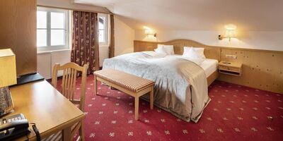 Doppelbett in der Juniorsuite mit rotem Teppich und Holzverkleidungen