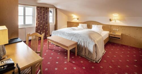 Doppelbett in der Juniorsuite mit rotem Teppich und Holzverkleidungen