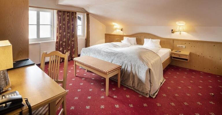 Doppelbett in der Juniorsuite mit rotem Teppich und Holzverkleidungen