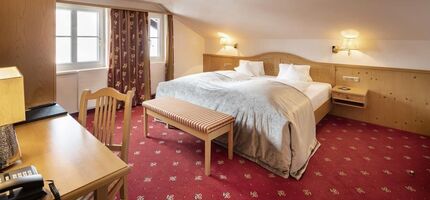 Doppelbett in der Juniorsuite mit rotem Teppich und Holzverkleidungen