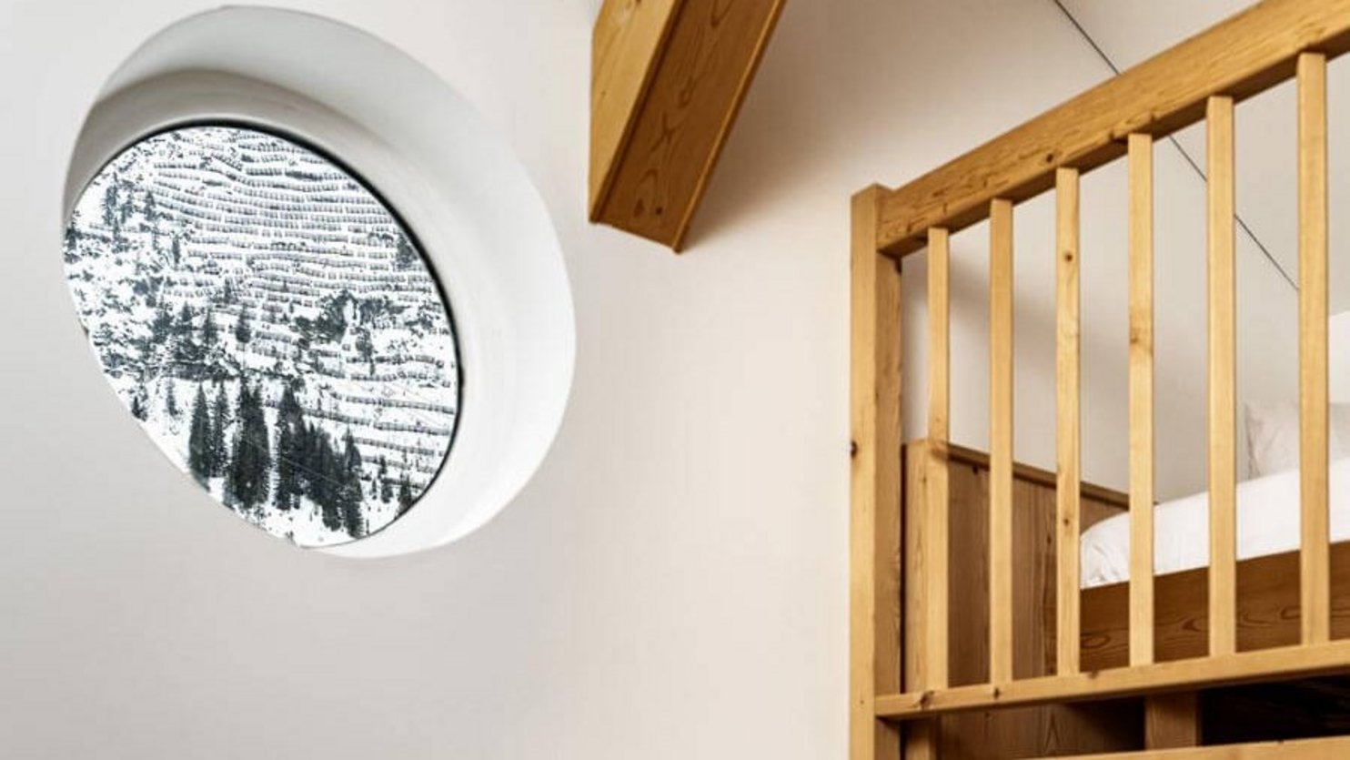 Interior space with a circular window overlooking snowy mountains and wooden features