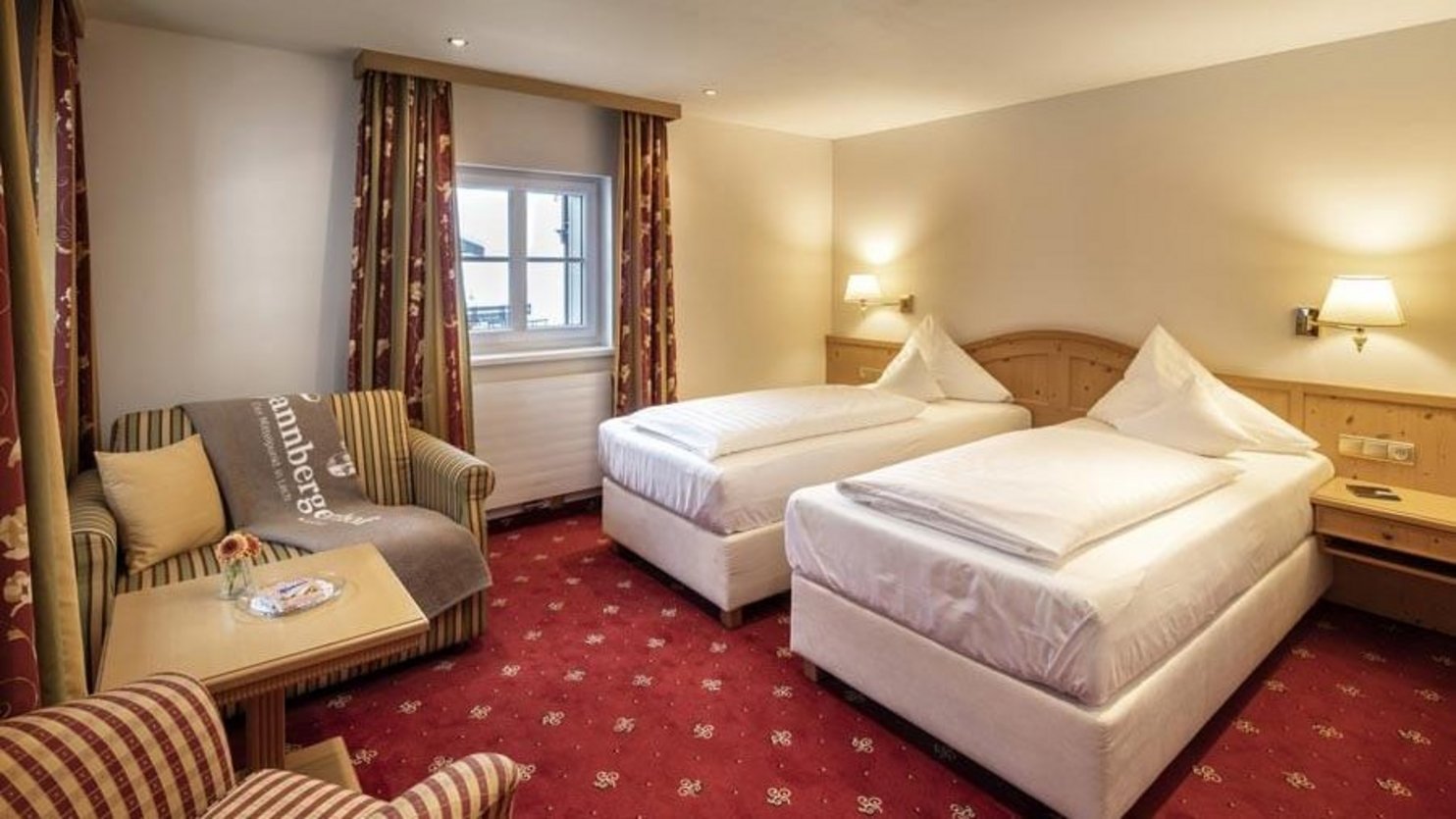 Hotel room with two twin beds and a comfortable seating area under warm lighting