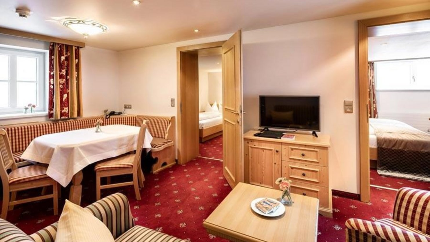 Hotel room featuring a living area with sofa and dining table, separate bedroom visible through an open door