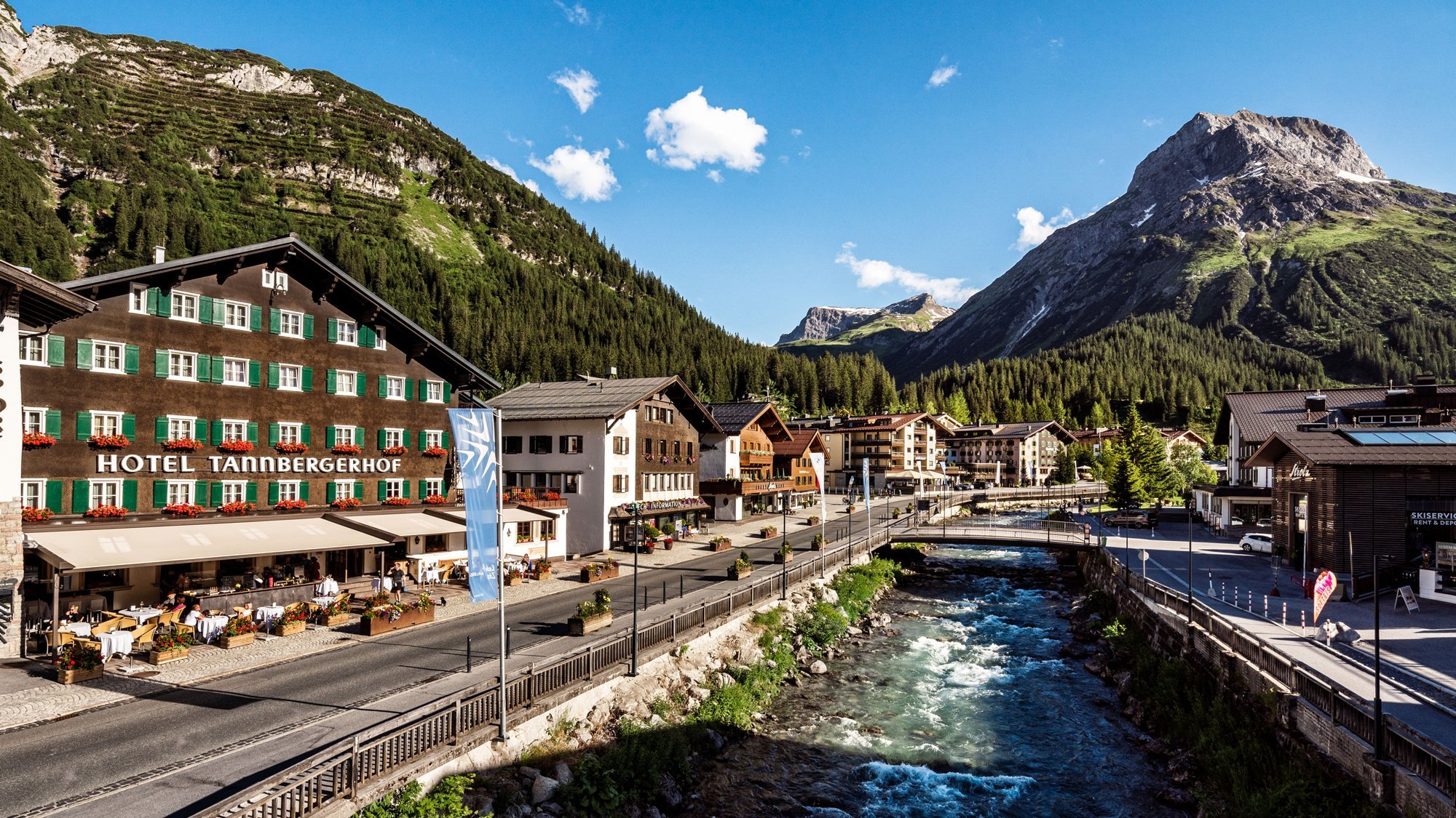 Malersches Alpendorf mit Hotel und Blick auf Berge und Flusslauf in der Naturkullisse.