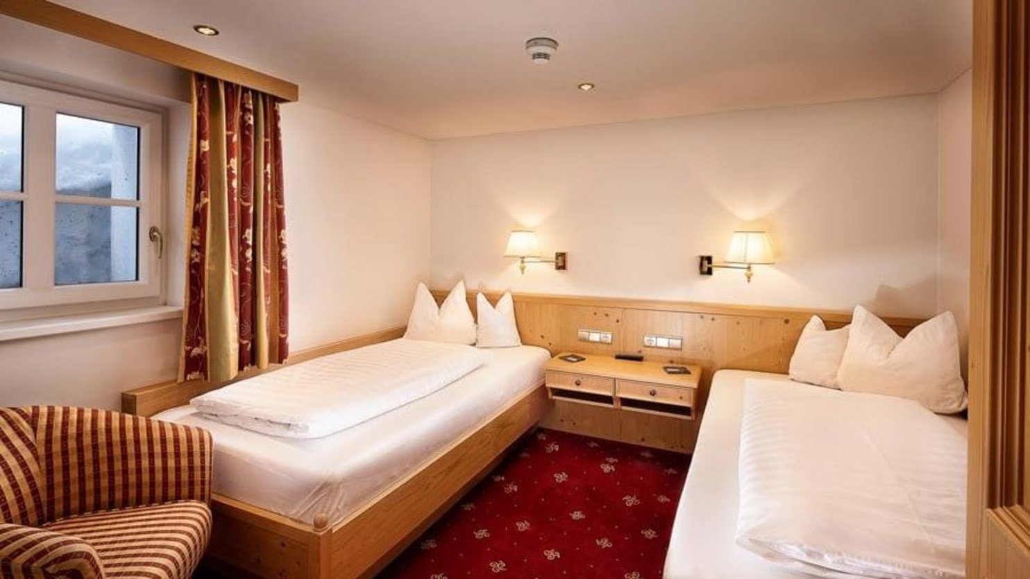Interior view of a hotel room featuring two single beds and a patterned armchair
