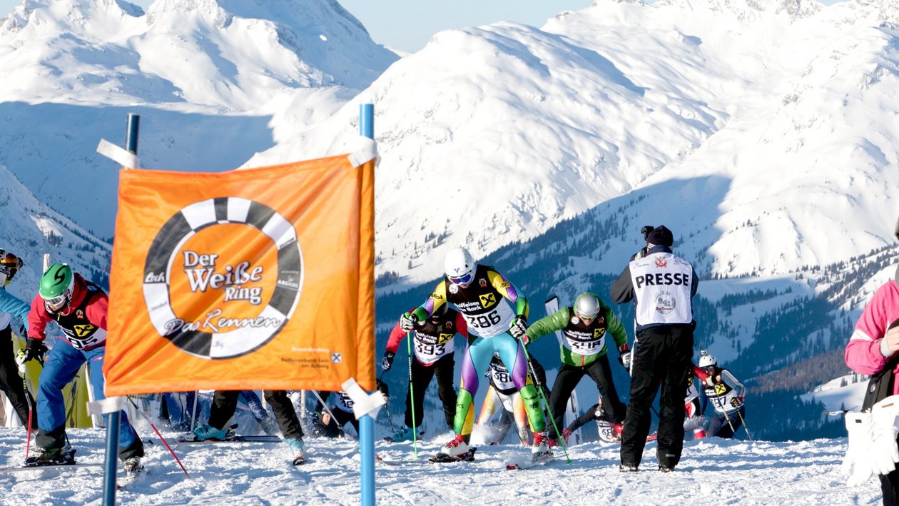 Skiwettkampf in den Alpen Gruppe von Skifahrern bereitet sich auf ein Rennen an einer schneebedeckten Piste vor, orange Banner im Vordergrund.