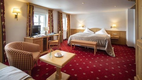 Geräumiges Hotelzimmer mit großem Bett, Sitzbereich und Schreibtisch mit Computer