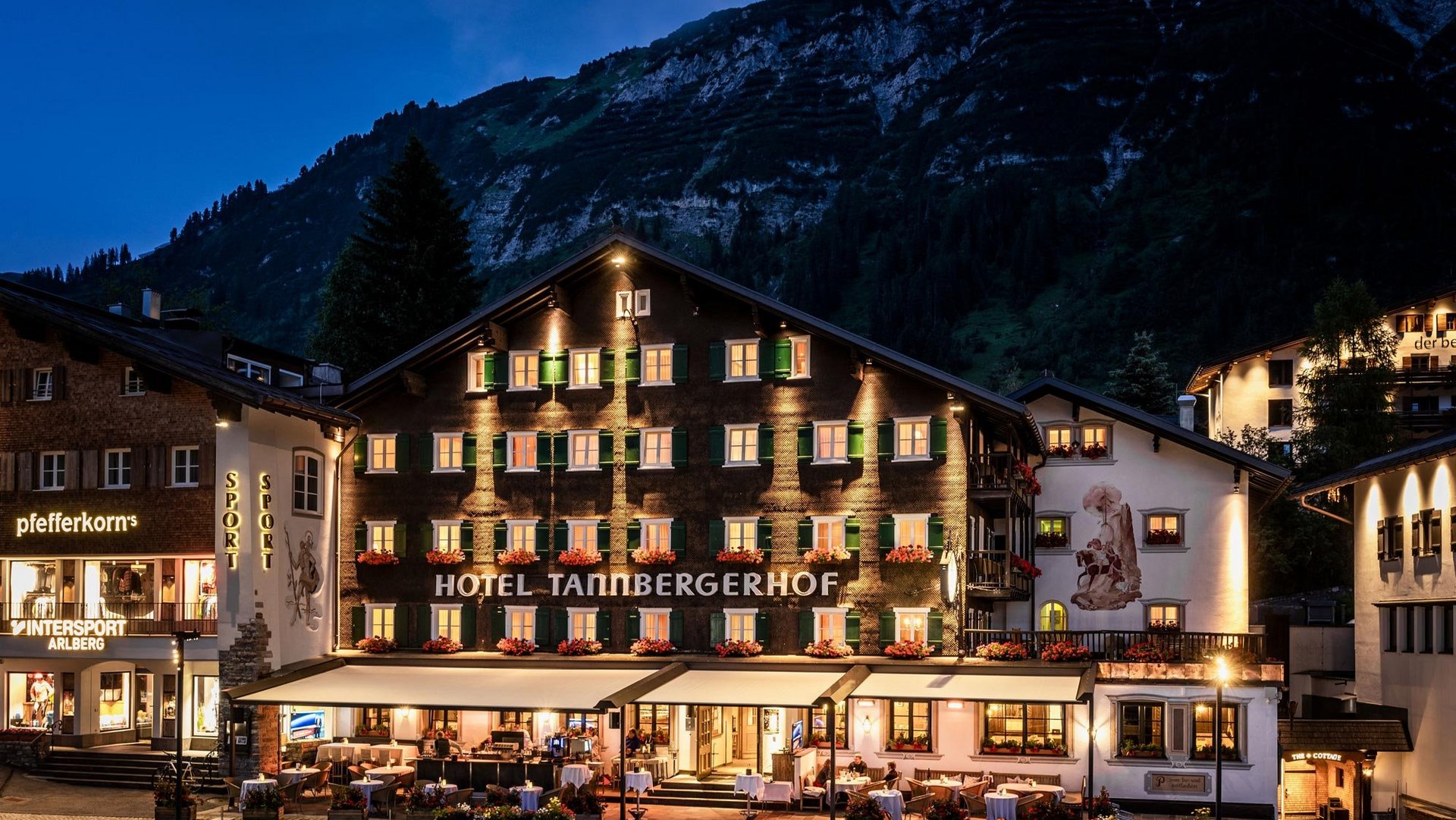 Außenansicht des Hotel Tannbergerhof nachts, erleuchtet und umgeben von den Alpen