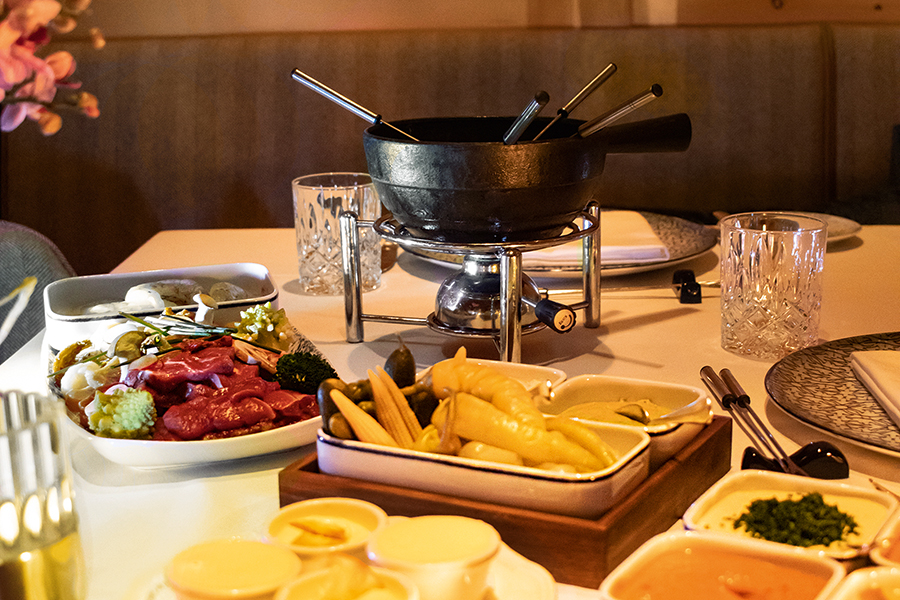 Fondue-Set mit Fleisch, Gemüse, Saucen und Beilagen auf einem gedeckten Tisch im Tannbergerhof in Lech © Robert Stocker