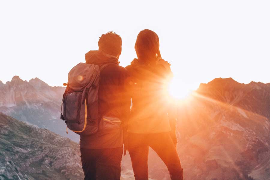 Zwei Wanderer mit Rucksack blicken auf die Vorarlberger Berge im Sonnenuntergang © Daniel Zangerl
