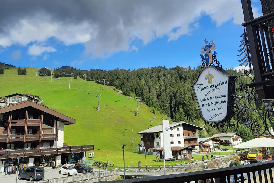 View of a verdant slope with hiking and ski lifts and a sign for the Hotel Tannbergerhof visible in the foreground